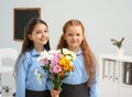 Happy schoolgirls with bouquet in classroom.