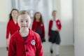 Happy schoolgrirl with Down syndrome in uniform walking in scool corridor with classmates behind her. Royalty Free Stock Photo