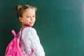 happy schoolkid smiling while standing with backpack on green .