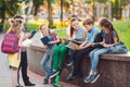 Happy Schoolmates Portrait. Schoolmates seating with books in a wooden bench in a city park and studying on sunny day.