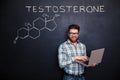 Happy scientist standing over chalkboard background and using laptop