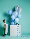 Happy laughing kid boy looks at bunch of blue balloons for birthday party flying out of white box he has just opened Royalty Free Stock Photo