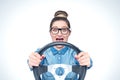 Happy screaming young girl with glasses and car steering wheel, front view, auto concept