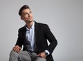 Happy seated businessman in black suit looks up to side