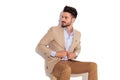 Happy seated businessman buttoning coat and looks to side