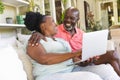 Happy senior african american couple on couch using laptop and embracing in sunny living room Royalty Free Stock Photo