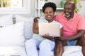 Happy senior african american couple on couch using laptop and embracing in sunny living room Royalty Free Stock Photo