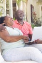 Happy senior african american couple on couch using laptop and laughing in sunny living room Royalty Free Stock Photo