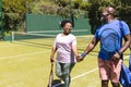 Happy senior african american couple with rackets walking holding hands on sunny grass tennis court Royalty Free Stock Photo