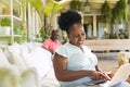 Happy senior african american couple in sunny living room, the woman on couch using laptop Royalty Free Stock Photo
