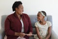 Happy senior african american grandmother sitting on couch beside smiling granddaughter using tablet Royalty Free Stock Photo
