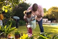 Happy senior african american man and his granddaughter watering plants in sunny garden Royalty Free Stock Photo