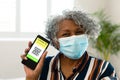 Happy senior african american woman wearing face mask showing covid qr code on smartphone Royalty Free Stock Photo