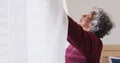 Happy senior african american woman widening curtains in bedroom