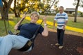 Happy senior American couple around 70 years old enjoying at swing park with husband pushing wife smiling and having fun Royalty Free Stock Photo