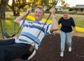 Happy senior American couple around 70 years old enjoying at swing park with wife pushing husband smiling and having fun together Royalty Free Stock Photo