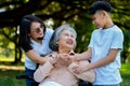 Happy senior Asian grandmother uses wheelchair with her daughter and grandchild in park, Grandson came to visit elderly