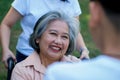 Happy senior Asian grandmother uses wheelchair with her daughter and grandchild in park, Grandson came to visit elderly