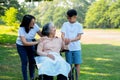 Happy senior Asian grandmother uses wheelchair with her daughter and grandchild in park, Grandson came to visit elderly