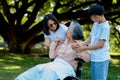 Happy senior Asian grandmother uses wheelchair with her daughter and grandchild in park, Grandson came to visit elderly