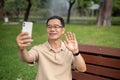 A happy senior Asian man is talking on a video call with his daughter while relaxing in a green park Royalty Free Stock Photo