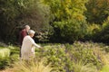 Happy senior biracial couple holding hands and touching flowers in garden at home, copy space