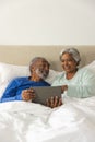 Happy senior biracial couple lying in bed using tablet at home, copy space Royalty Free Stock Photo