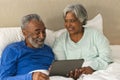 Happy senior biracial couple lying in bed using tablet at home Royalty Free Stock Photo