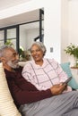 Happy senior biracial couple sitting on couch and using tablet at home, copy space Royalty Free Stock Photo