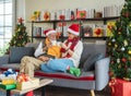 Happy Senior Caucasian couple in Santa hat sitting together on sofa couch holding and clinking hot drink cup at home with Royalty Free Stock Photo