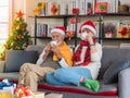 Happy Senior Caucasian couple in Santa hat sitting together on sofa couch holding hot drink at home with decorated Christmas tree Royalty Free Stock Photo