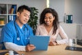 Happy senior chinese man with tablet consulting young african american female patient in clinic office interior