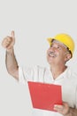 Happy senior constructor holding clipboard while gesturing thumbs up over gray background