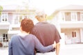 Happy senior couple from behind looking at front of house and car. Warm tone with sunlight.