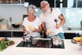 Happy senior couple dancing while cooking together at home - Mature people having fun preparing the lunch - Joyful elderly Royalty Free Stock Photo