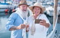 Happy senior couple doing selfie, cheering with champagne on a sailboat during anniversary vacation - Joyful elderly lifestyle,