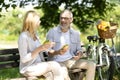 Happy Senior Couple Eating Sandwiches While Sitting On Bench In Park Royalty Free Stock Photo