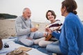 Happy senior couple with granddaughter sitting on blanket and having picnic outdoors on beach by sea. Royalty Free Stock Photo