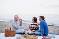 Happy senior couple with granddaughter sitting on blanket and having picnic outdoors on beach by sea. Royalty Free Stock Photo