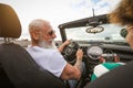 Happy senior couple having fun taking photo with old vintage camera while driving on new convertible car during road trip Royalty Free Stock Photo