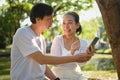 Happy senior couple having fun using mobile phone while sitting in the park on beautiful spring day. Royalty Free Stock Photo