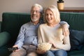 Happy senior couple holding remote control snack laughing watching tv Royalty Free Stock Photo