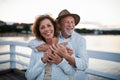 Happy senior couple hugging outdoors on pier by sea, looking at camera. Royalty Free Stock Photo