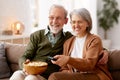 Happy senior couple husband and wife eating popcorn and watching TV at home