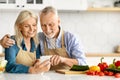 Happy senior couple looking at smartphone screen and cooking together Royalty Free Stock Photo