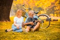 happy senior couple in love playing acoustic guitar in park under big tree with bike in autumn