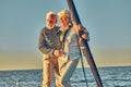 Happy senior couple in love, retired man and woman standing on the side of sail boat or yacht deck floating in sea