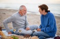 Happy senior couple in love sitting on blanket drinking wine and playing chess outdoors on beach. Royalty Free Stock Photo