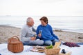 Happy senior couple in love sitting on blanket and embracing when having picnic outdoors on beach Royalty Free Stock Photo
