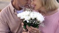 Happy senior couple nuzzling, holding flowers bunch together, anniversary date